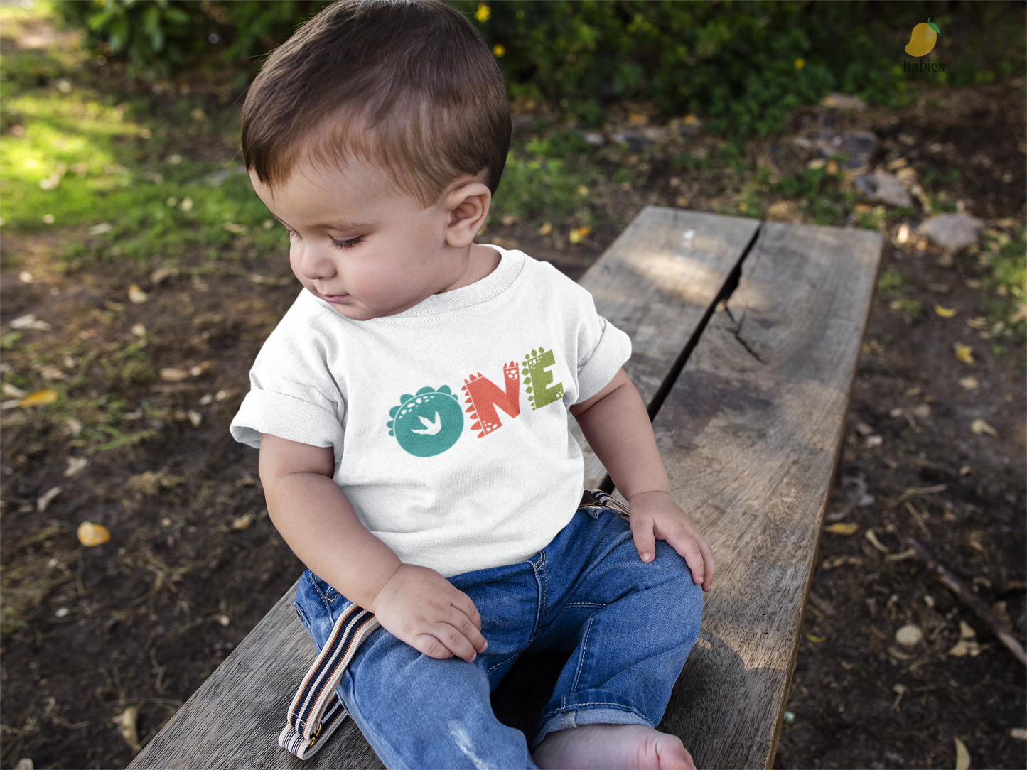 Toddler wearing a black t-shirt with "One" in a yellow dinosaur font.