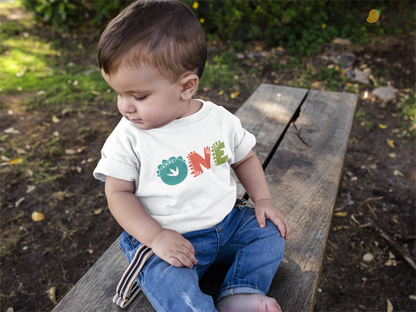 Toddler wearing a black t-shirt with "One" in a yellow dinosaur font.
