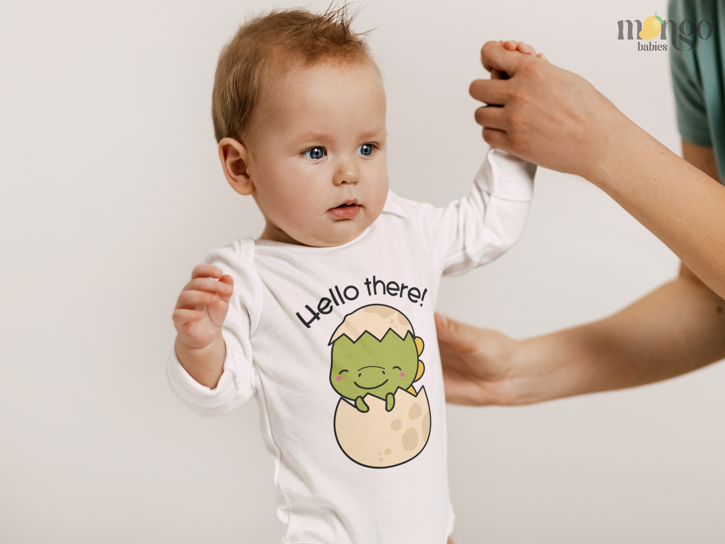 Cute dinosaur hatching from an egg with “Hello There” text printed on baby onesie and kids’ t-shirts.
