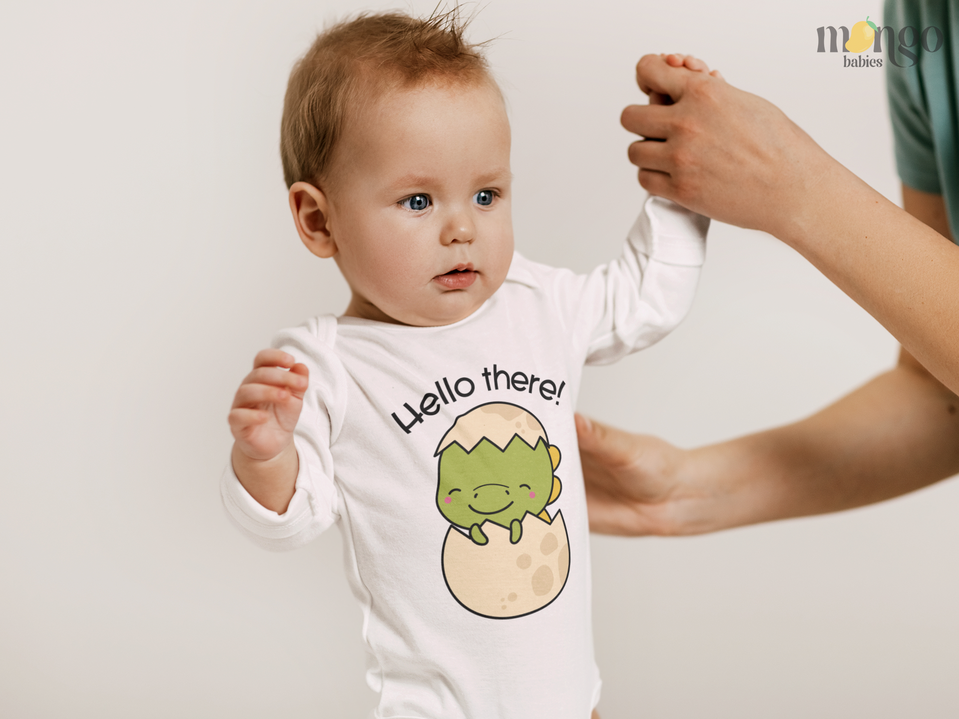 Cute dinosaur hatching from an egg with “Hello There” text printed on baby onesie and kids’ t-shirts.
