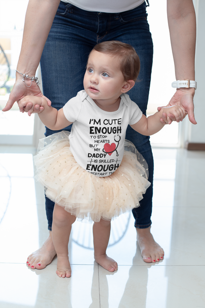 Cute baby onesie and kids’ shirt with the text “I’m cute enough to stop hearts but my daddy is skilled enough to restart them” in playful font.
