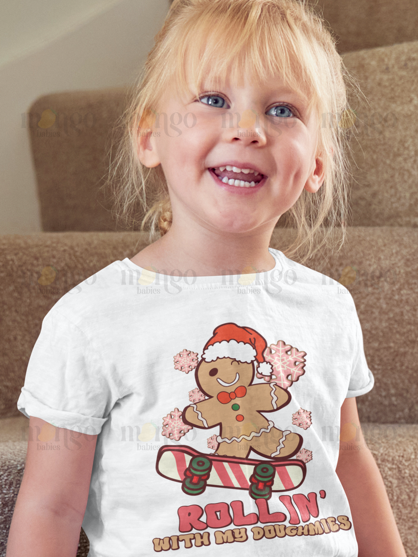 Christmas gingerbread man on skateboard with “rollin' with my doughmies” text on baby onesie, kids t-shirt, unisex adult shirt, and children sweatshirt.