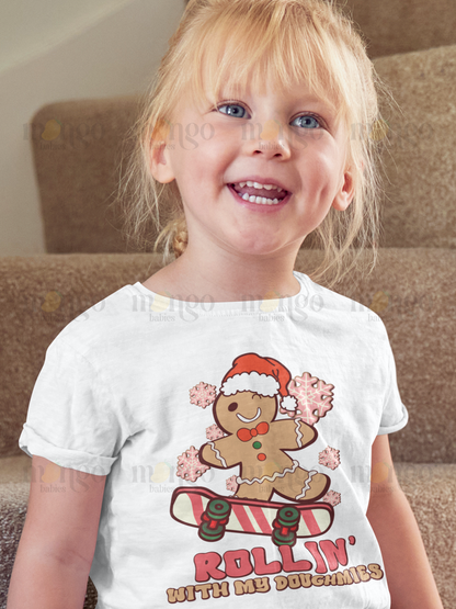 Christmas gingerbread man on skateboard with “rollin' with my doughmies” text on baby onesie, kids t-shirt, unisex adult shirt, and children sweatshirt.