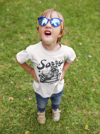 Cute raccoon sitting on a couch with text “Sorry Got Plans” printed on baby onesie, toddler t-shirt, and kids’ shirt.
