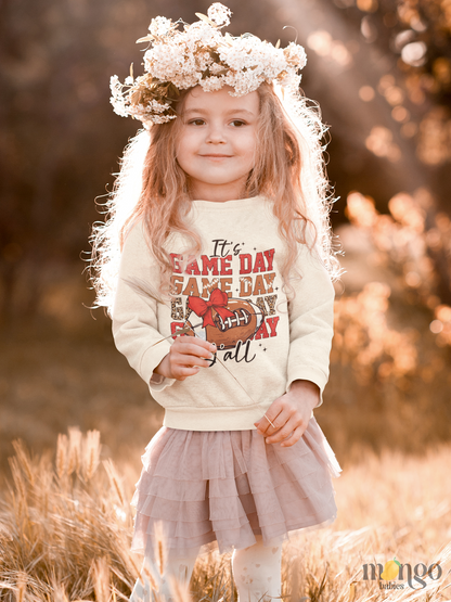 Football graphic with red bow and “It’s Game Day Y’all” printed on baby bodysuit, kids’ t-shirt, sweatshirt, and unisex adult shirt.