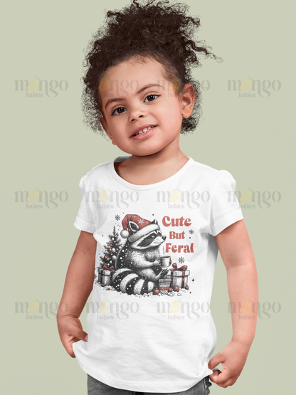 Christmas shirt with cute raccoon wearing Santa hat and text "Cute but Feral," available as baby bodysuit, kids t-shirt, adult tee, and children sweatshirt.