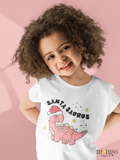 Pink Christmas dinosaur graphic with Santa hat and “Santa Saurus” text printed on baby bodysuit, kids’ t-shirt, sweatshirt, and adult unisex shirt.